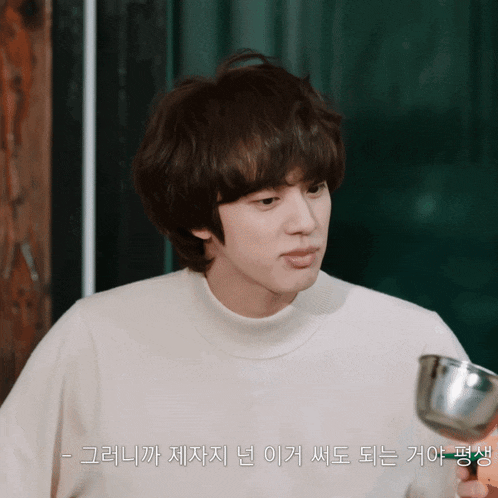 a man in a white sweater is holding a ladle with korean writing on it