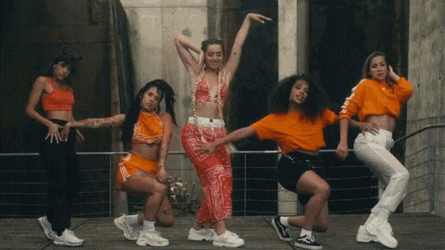 a group of women are dancing together and one of them is wearing an orange shirt