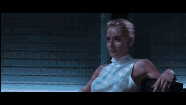 a woman in a white turtleneck sits in a dark room