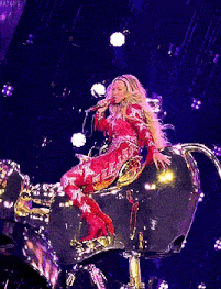a woman in a red jumpsuit is singing into a microphone while sitting on a drum .