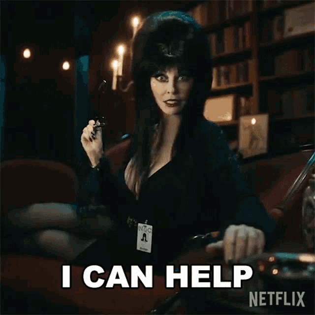 a woman in a black dress is sitting on a couch holding a pair of glasses and saying i can help .