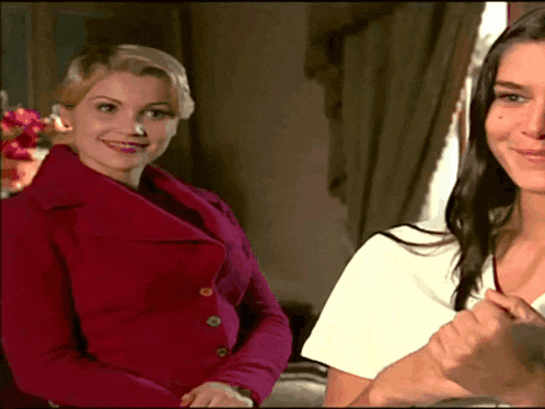 a woman in a red jacket smiles next to another woman in a white shirt