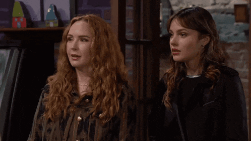 two women with red hair are standing next to each other in front of a brick wall .