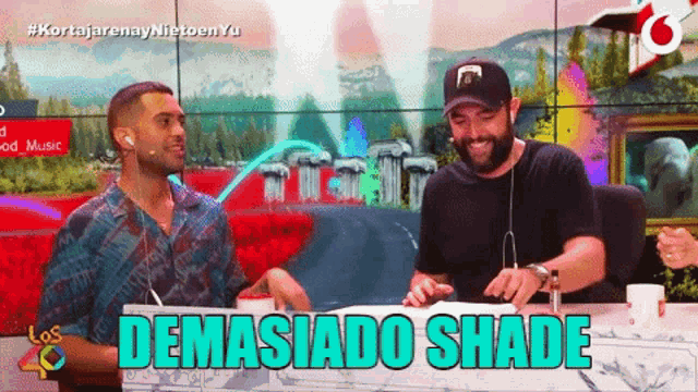 two men are sitting at a table with the words demasiado shade written on it