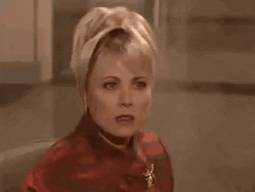 a woman is wearing a red coat and a brooch and making a funny face .