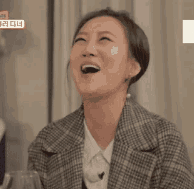 a woman in a plaid jacket is laughing with her mouth open in front of a sign that says ' a ' on it