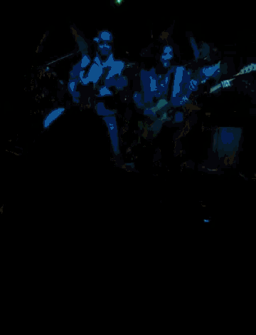a man playing a guitar in a dark room with a green light behind him