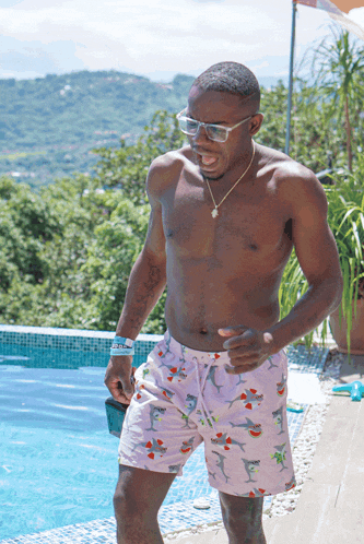 a shirtless man wearing pink swim trunks with sharks on them is standing next to a pool
