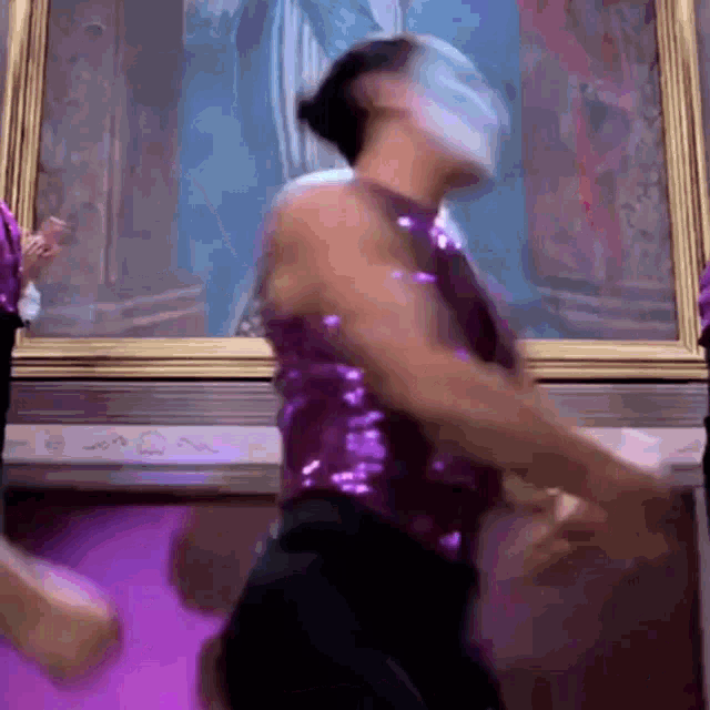 a man in a purple sequined top is dancing in front of a framed picture