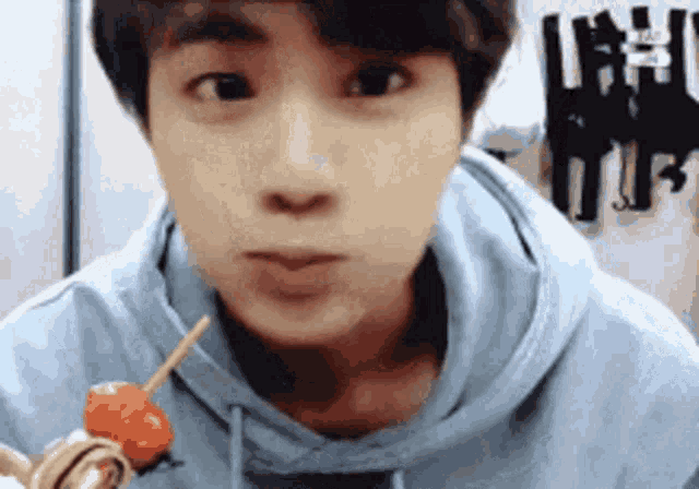 a man in a blue hoodie is holding a strawberry on a stick .