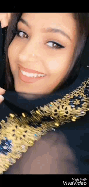 a woman wearing a black and gold dress is smiling and covering her face with her hand .