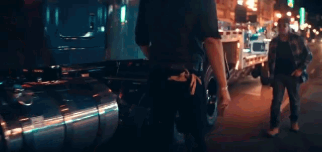 two men are walking down a street at night and one has a gun in his belt