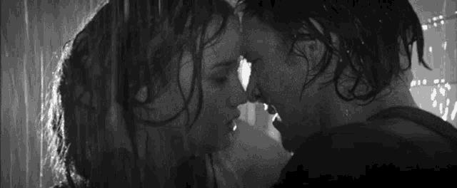 a man and woman are kissing in the rain in a black and white photo .