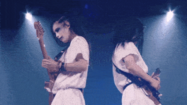 two women in white dresses playing guitars on stage