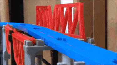 a blue and red toy train track with a red bridge in the background .