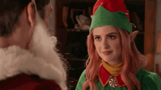 a woman dressed as an elf is looking at a man dressed as santa claus .