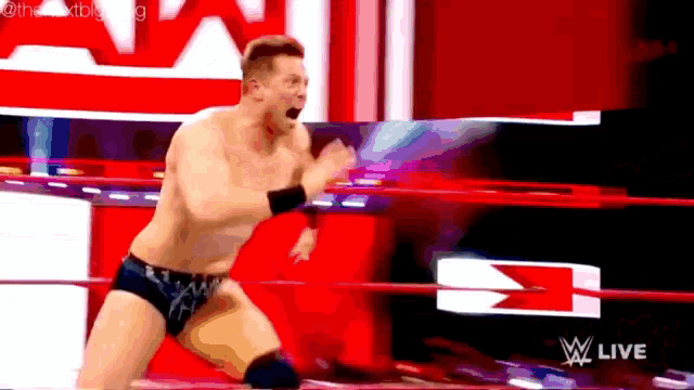 a shirtless wrestler in a wrestling ring with a w live sign in the background