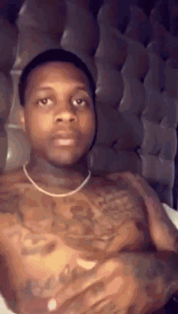 a shirtless man is sitting on a bed with his arms crossed and a necklace around his neck .