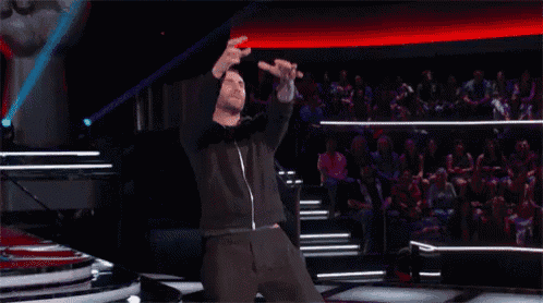 a man in a black jacket stands on a stage with his arms in the air