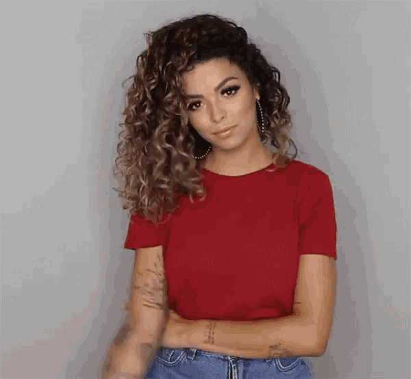 a woman with curly hair wearing a red shirt and jeans