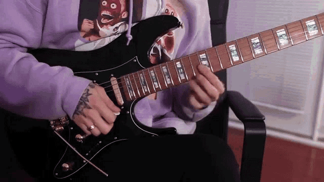 a person wearing a purple sweatshirt is playing a guitar