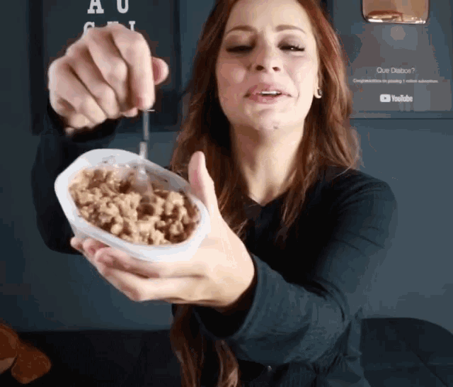 a woman is holding a container of food with a spoon in her hand
