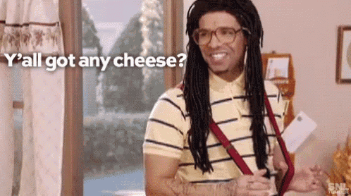 a man with dreadlocks and glasses is standing in front of a window and saying `` y all got any cheese ? ''