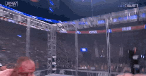 a man with blood on his face is standing in a cage with a aew logo on the bottom right corner