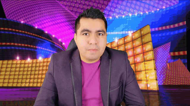 a man in a purple suit and a purple shirt is sitting in front of a stage