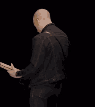 a man in a black jacket is playing a guitar on a black background