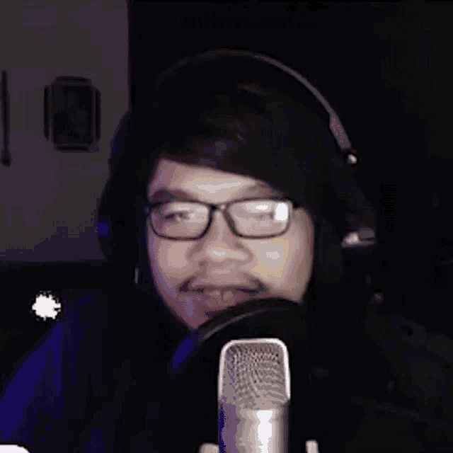 a man wearing glasses and headphones is standing in front of a microphone .