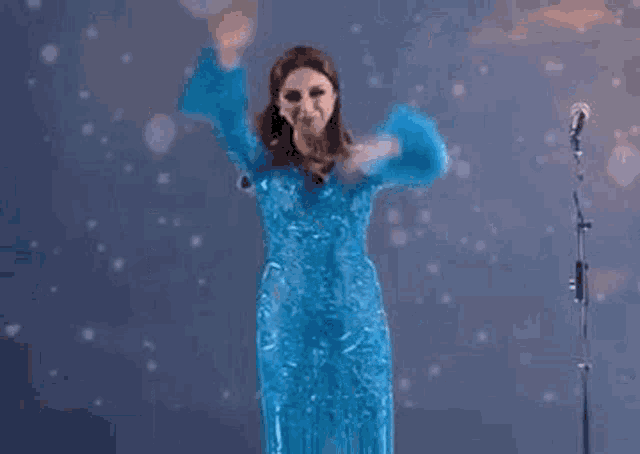 the woman is wearing a blue dress and dancing in front of a microphone .