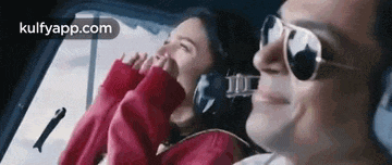 a man and a woman are sitting in a helicopter . the woman is wearing sunglasses and headphones .
