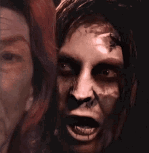 a close up of a zombie 's face with a woman 's face in the background .