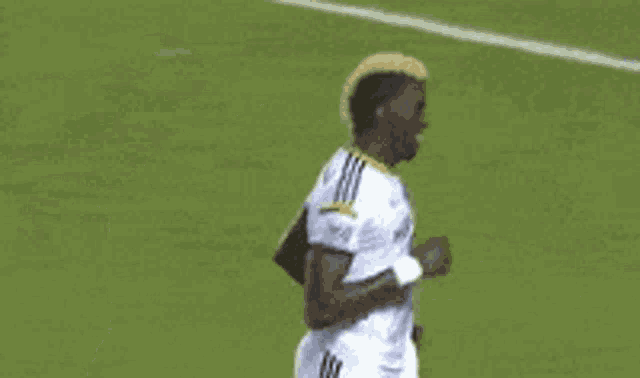 a soccer player wearing a hat is standing on a field with his hands in the air .