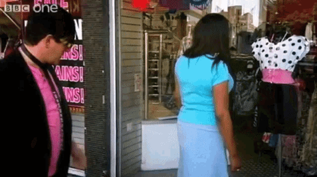a woman in a blue shirt stands in front of a sign that says ' bbc one ' on it