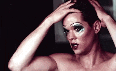 a shirtless man with makeup on his face is fixing his hair .