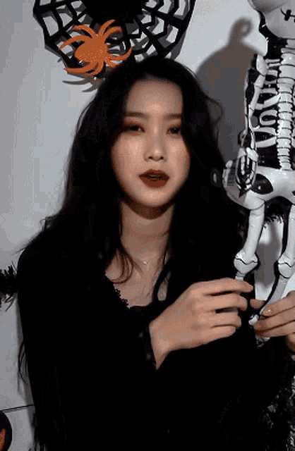 a woman in a black dress is holding a skeleton balloon in front of a spider web .