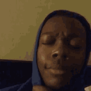 a close up of a person 's face with their eyes closed and a blue hoodie on .