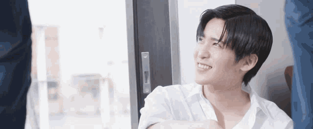 a young man is sitting in front of a window and smiling .