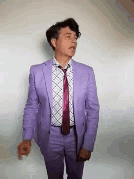 a man wearing a purple suit and tie is dancing .