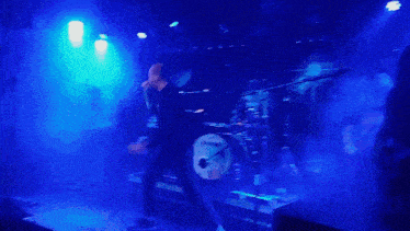 a man singing into a microphone on a stage with a drum set in the background