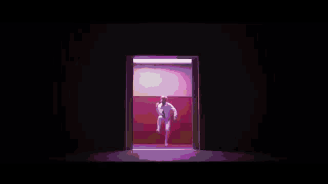a man in a white suit is dancing on a stage in front of a pink wall .