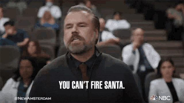 a man with a beard is standing in front of a crowd of people and says you can 't fire santa .