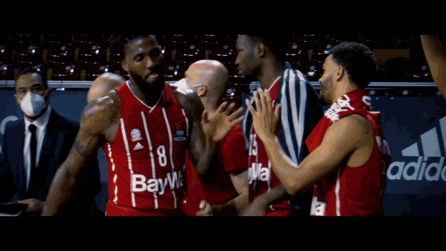 a basketball player with the number 8 on his jersey is surrounded by his teammates