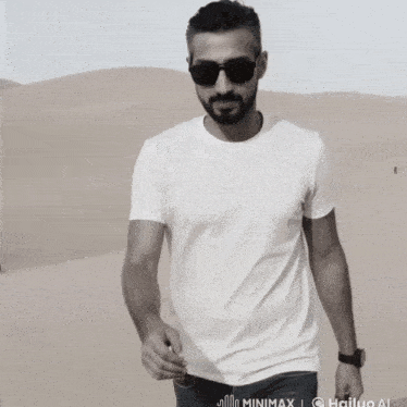 a man wearing sunglasses and a white t-shirt is standing in the desert