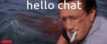 a man with a cigarette in his mouth is talking on a cell phone while a shark is behind him .