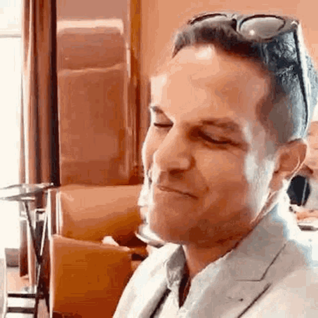 a man wearing sunglasses and a suit is smiling while sitting at a table in a restaurant .