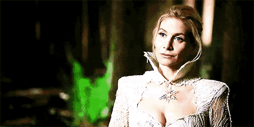 a woman in a white dress with a necklace around her neck is standing in a dark room .