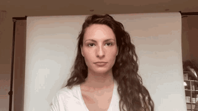 a woman with long brown hair is standing in front of a white backdrop .